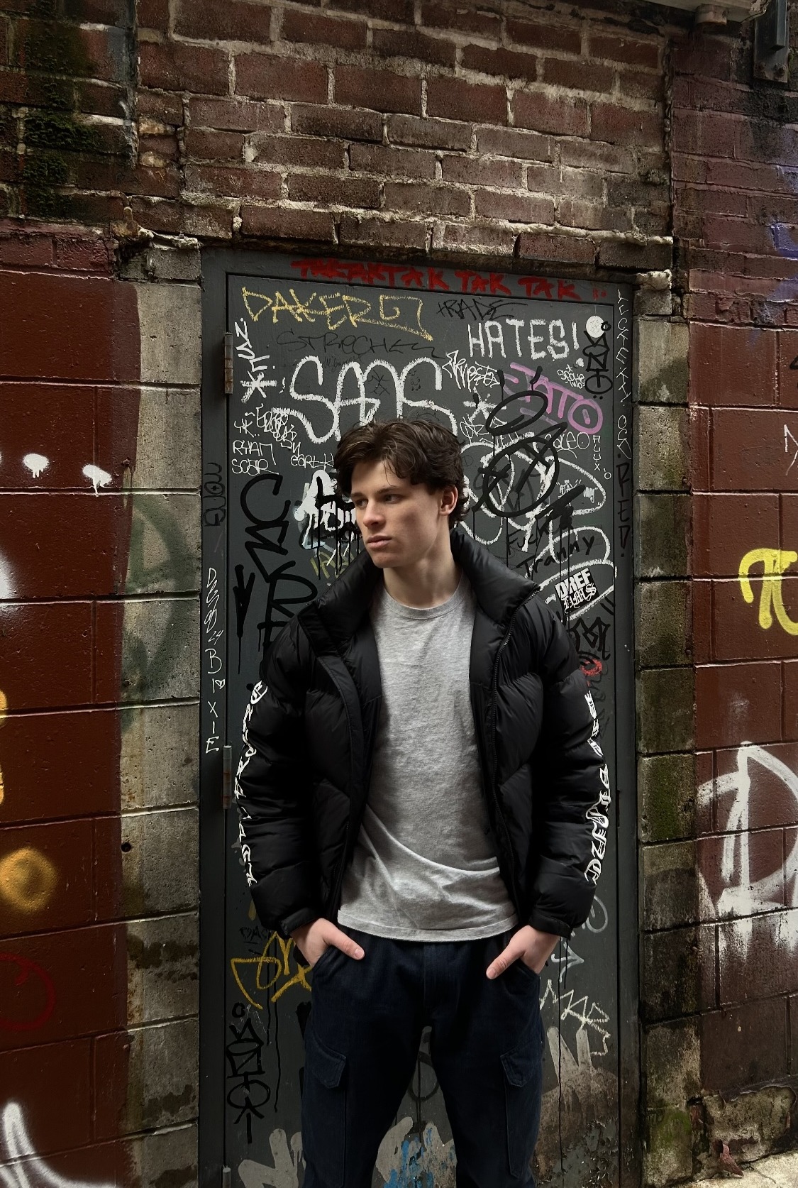 About - (Desc: Xander in Front of Graffitied Wall)